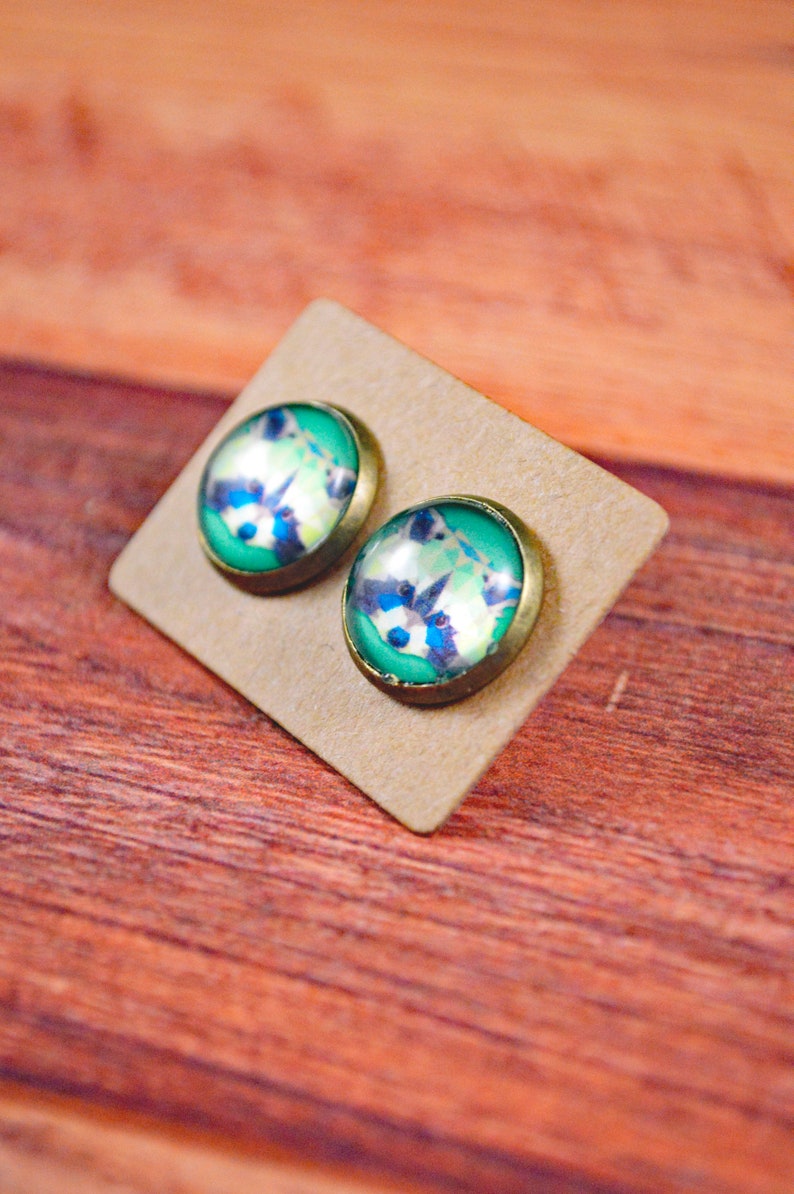 May include: A pair of round, green and white glass earrings with a raccoon design. The earrings are on a brown card.