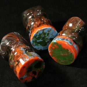 May include: Three round, clear glass bottle stoppers with a swirling pattern of orange, green, and blue paint.