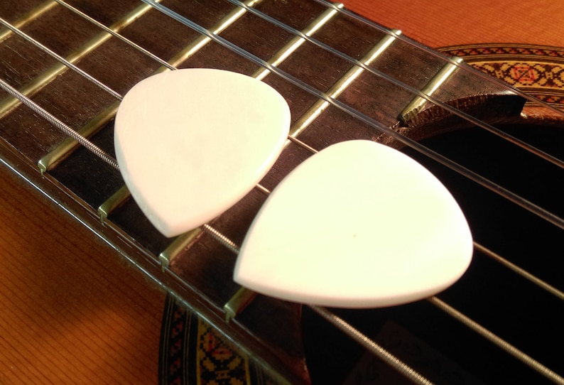 May include: Two white guitar picks on a brown acoustic guitar fretboard.