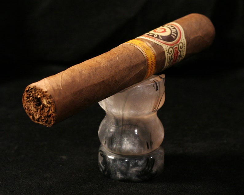 May include: A brown cigar with a gold and white band that reads "Don Carlos" is resting on a black and white marble ashtray.