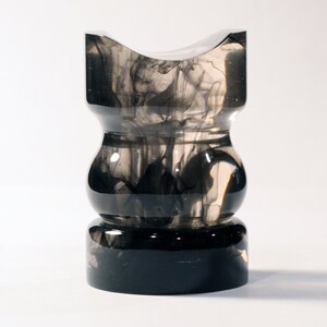 May include: A clear glass vase with black ink swirling inside. The vase has a wide base and a narrow neck.