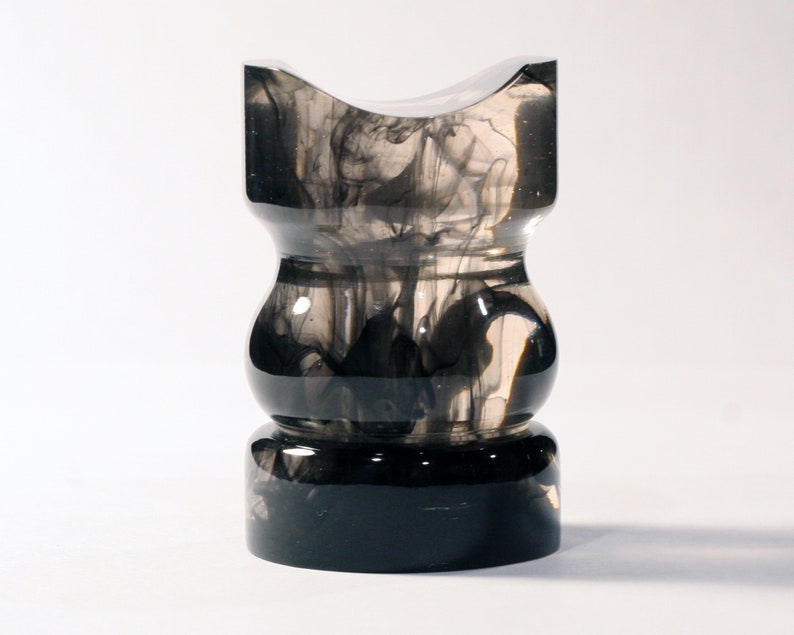 May include: A clear glass vase with black ink swirling inside. The vase has a wide base and a narrow neck.