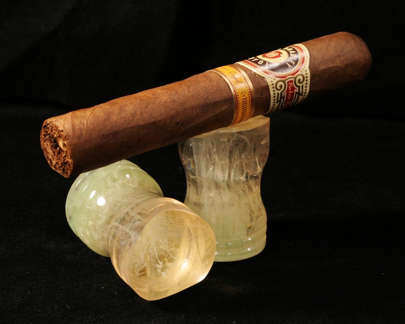 May include: A brown cigar with a gold and white band that reads "Don Francisco" is resting on two clear glass ashtrays with a white swirl design.