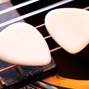 May include: Two white guitar picks on a brown guitar neck with copper strings.
