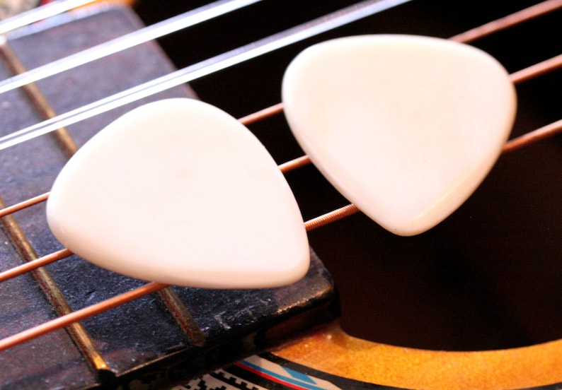 May include: Two white guitar picks on a brown guitar neck with copper strings.