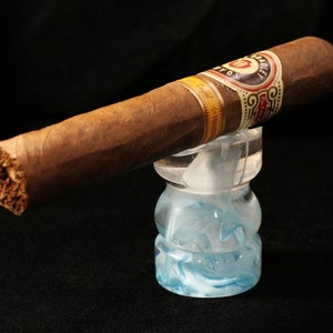 May include: A brown cigar with a gold and red band that says "Caridad" on a blue and white swirl glass cigar rest.