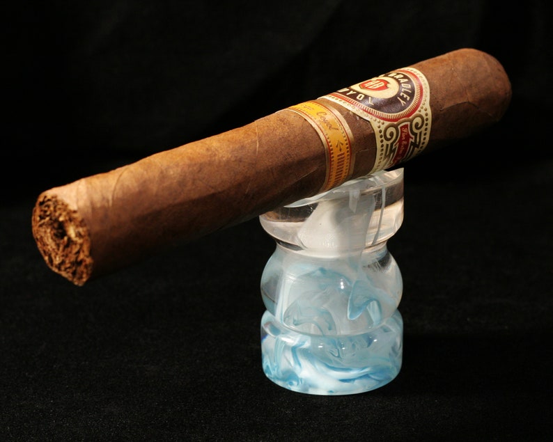 May include: A brown cigar with a gold and red band that says "Caridad" on a blue and white swirl glass cigar rest.