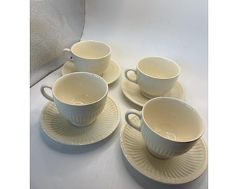 Op de afbeelding: Een set van vier off-white keramische theekopjes met bijpassende schoteltjes. Elke kop heeft een afgerond oortje en een geribbelde textuur aan de buitenkant. De schoteltjes hebben ook een bijpassend geribbeld patroon.