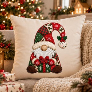 May include: A square cream-colored throw pillow featuring a central applique of a gnome. The gnome wears a patchwork hat in red and green with snowflake patterns, a white beard, and holds a green gift box with a red bow and white snowflakes.