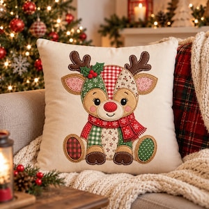 May include: A square throw pillow with a cream-colored fabric cover featuring a central applique of a cartoon reindeer. The reindeer is decorated with various red, green, and white fabric patches in plaid, floral, and snowflake patterns.