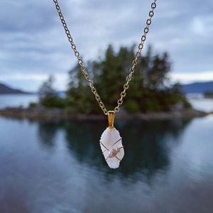 May include: A gold chain necklace with a white stone pendant. The stone is wrapped with gold wire and has a small pearl accent.