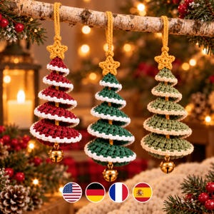 May include: Three crocheted Christmas tree ornaments hanging from a branch. Each tree features tiered layers in red, dark green, and light green with white trim, topped with a yellow crocheted star and a small gold bell at the base.