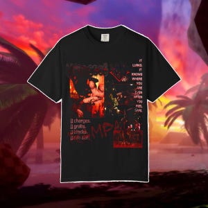 Puede incluir: Una camiseta negra de manga corta con un estampado gráfico en tonos rojos y oscuros. El texto dice: IT LURKS. IT KNOWS WHERE YOU ARE EVEN WHEN YOU FEEL SAFE. It charges. It grabs. It blocks. It can see!