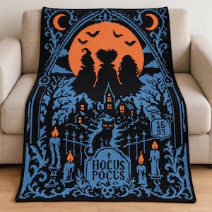 Pode incluir: Uma manta de crochê retangular com fundo preto e detalhes em azul e laranja. O design exibe três silhuetas contra uma grande lua laranja, um gato preto, velas acesas, árvores e uma lápide com a inscrição Hocus Pocus 1693.