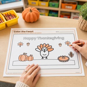 May include: A white paper placemat with the text Color the Feast and Happy Thanksgiving, featuring line art of a turkey, pumpkins, a pie, acorns, and leaves. The placemat has orange accents and is partially colored with an orange crayon.