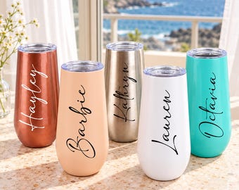 May include: Five stainless steel stemless champagne flutes with clear lids, each featuring a unique name in black or white script: Hayley, Barbie, Kathryn, Lauren, and Octavia. The tumblers come in metallic copper, matte peach, metallic gold, white, and bright turquoise.