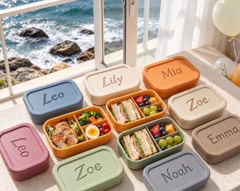 Puede incluir: Una colección de fiambreras rectangulares de silicona en varios colores, incluyendo azul, beige, naranja, verde y rosa. Cada tapa tiene grabado un nombre como Leo, Lily, Mia, Zoe, Emma o Noah. Dos cajas abiertas muestran compartimentos con sándwiches, pollo en rodajas, huevos cocidos, uvas y bayas.
