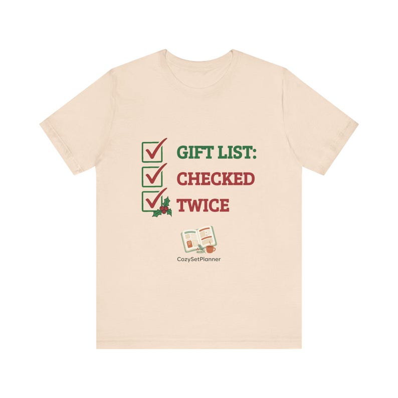 A cream mockup of a short-sleeve t-shirt with the checked it twice Christmas design showing three green checkboxes, the text "GIFT LIST: CHECKED TWICE," and a small open planner illustration.