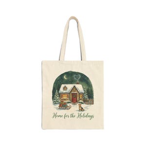 A natural beige canvas tote bag in the Natural color variant showing the snowy Christmas cottage "Home for the Holidays" print on a plain light-gray background.