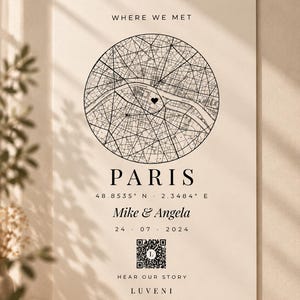 Könnte beinhalten: Ein cremefarbenes vertikales Poster mit einer kreisförmigen schwarz-weißen Karte von Paris und einem Herzsymbol. Der Text umfasst WHERE WE MET, PARIS, 48.8535 N 2.3484 E, Mike & Angela, 24 07 2024, einen QR-Code, HEAR OUR STORY und den Markennamen LUVENI.