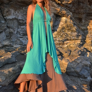 May include: A woman wearing a teal blue halter dress with a brown skirt standing on a rocky surface.
