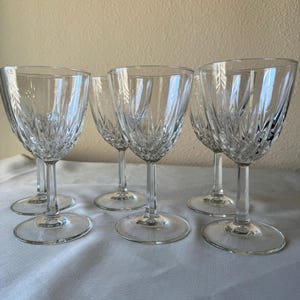 May include: A set of five clear glass wine glasses featuring a vertical ribbed pattern on the lower portion of the bowl, a slender stem, and a circular base. The glasses are arranged in a group, showcasing the transparent material and texture.