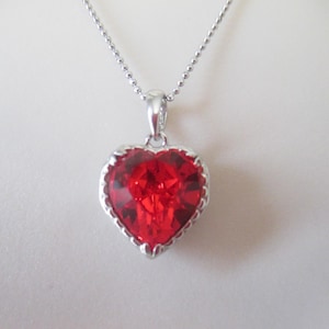 May include: A silver chain necklace with a red heart-shaped pendant. The pendant has a detailed silver border.
