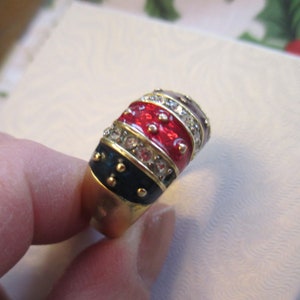 May include: A gold ring with a red, black, and white enamel design. The ring is set with clear rhinestones.