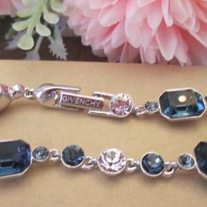 May include: Silver-toned bracelet featuring a series of blue and clear crystals. The bracelet has a clasp with the brand name "Givenchy" engraved on it. The crystals are in various shapes and sizes.