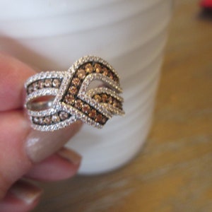 May include: A silver ring with a wave-like design set with small brown and white diamonds.
