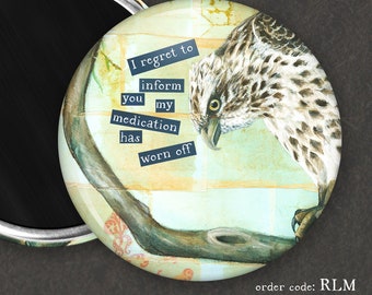 May include: A round magnet with a black mirror surface on one side and a colourful illustration of a bird on a branch on the other side. The illustration includes the text "I regret to inform you my medication has worn off".