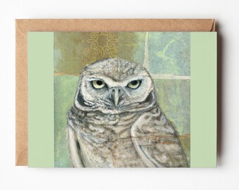 May include: A green and brown card with a painting of an owl with yellow eyes. The owl is looking directly at the viewer.