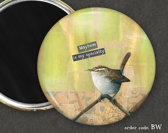 May include: A round magnet with a watercolor background featuring a small brown bird perched on a branch. The text "Mayhem is my specialty" is written in black on a white background.