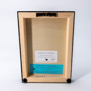 May include: A wooden frame with a black mat and a certificate of authenticity for a 5x7 inch print. The certificate is blue and white and includes the artist's name, Erin M. Linton, and the year 2022. The print is titled "Orphan Girl Fine Art" and is a gicl&eacute;e print. The certificate also includes the artist's signature and the number 21063.
