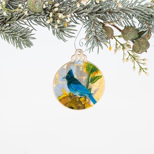 May include: A wooden Christmas ornament featuring a blue jay perched on a sunflower. The ornament is painted with a vintage style illustration and has a gold leaf background.