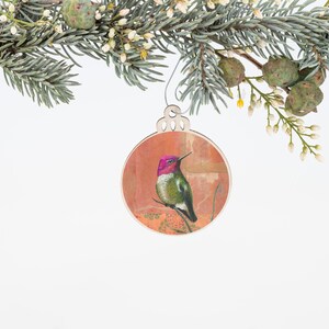 May include: A wooden Christmas ornament featuring a hummingbird with a pink head and green body, perched on a branch against a colorful background.