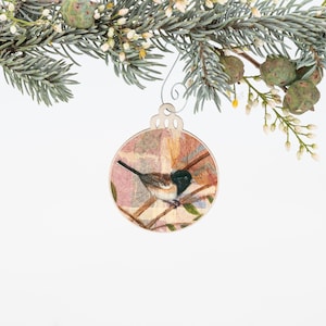 May include: A round wooden ornament with a delicate floral design and a small bird perched on a branch. The ornament is painted in shades of pink, brown, and green.