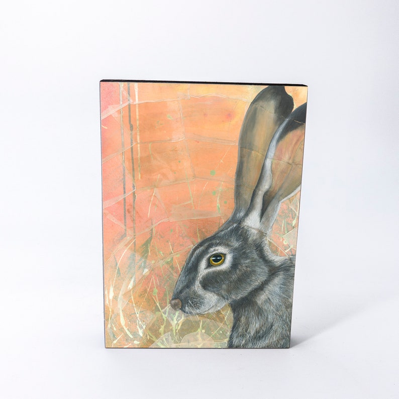 May include: A painting of a black-tailed jackrabbit with a yellow eye, set against a background of orange, pink, and white abstract shapes.