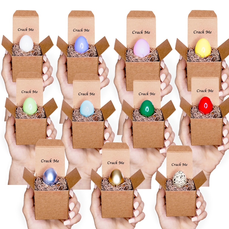 May include: Twelve small cardboard boxes with lids open, each containing a colorful Easter egg. The boxes are labeled "Crack Me" and are arranged in three rows of four boxes.