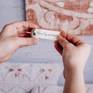 May include: A small, speckled egg with a white paper note inside. The note reads "We're Egg-specting!"