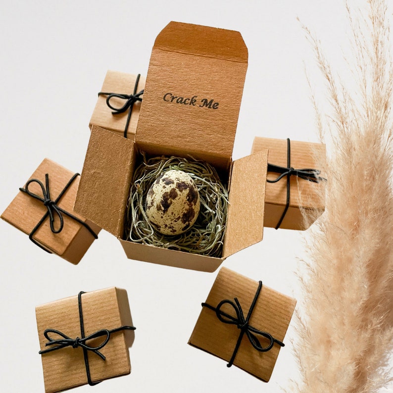 May include: A set of six small brown boxes with black ribbon tied around them. One box is open and contains a quail egg with the words "Crack Me" printed on the box.