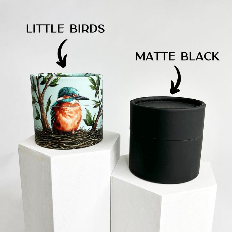 May include: Two round cardboard containers. One container is black and the other has a colorful design of a bird on a blue background. The text "LITTLE BIRDS" is above the container with the bird design. The text "MATTE BLACK" is above the black container.