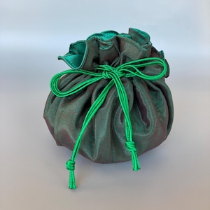 May include: A round, dark green pouch with a drawstring closure. The pouch is made of a shimmering fabric with a hint of red. The drawstring and the interior lining are a bright green color. The pouch is gathered at the top.