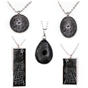 May include: Five silver necklaces with black glass pendants featuring a white spiderweb design. The pendants are in different shapes, including round, teardrop, and rectangular.