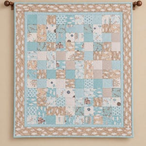 May include: A rectangular patchwork quilt featuring a grid of squares in light blue, beige, and white. The fabric patterns include illustrations of castles, hot air balloons, clouds, and small geometric prints, framed by a beige cloud-patterned border.