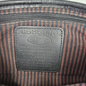 May include: Interior view of a black leather handbag. The lining features brown and black vertical stripes. A black leather tag displays the Brighton logo and the text "The Brighton Collection handbags are individually crafted in China from quality leathers."