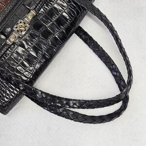 May include: Black leather handbag with a crocodile-skin texture. The bag features braided handles and a decorative silver clasp with a square, green stone. The top of the bag is brown leather.