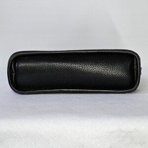 May include: A black leather handbag with a textured surface. The bag has a rectangular shape with rounded edges and a smooth, dark border. The bag is designed to be carried by hand or over the shoulder.