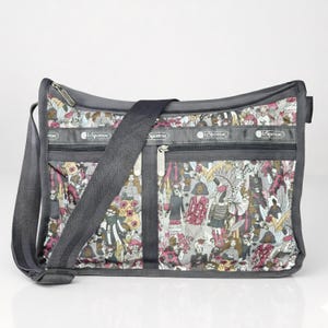 May include: Gray messenger bag with a colorful pattern of figures and floral elements. The bag has a long, adjustable strap and multiple zippered compartments. The brand name "LeSportsac" is visible on the bag.
