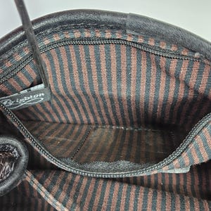 May include: Interior view of a black leather handbag. The lining features brown and black vertical stripes. A small zippered pocket is visible. The brand name "Brighton" is visible on a tag.